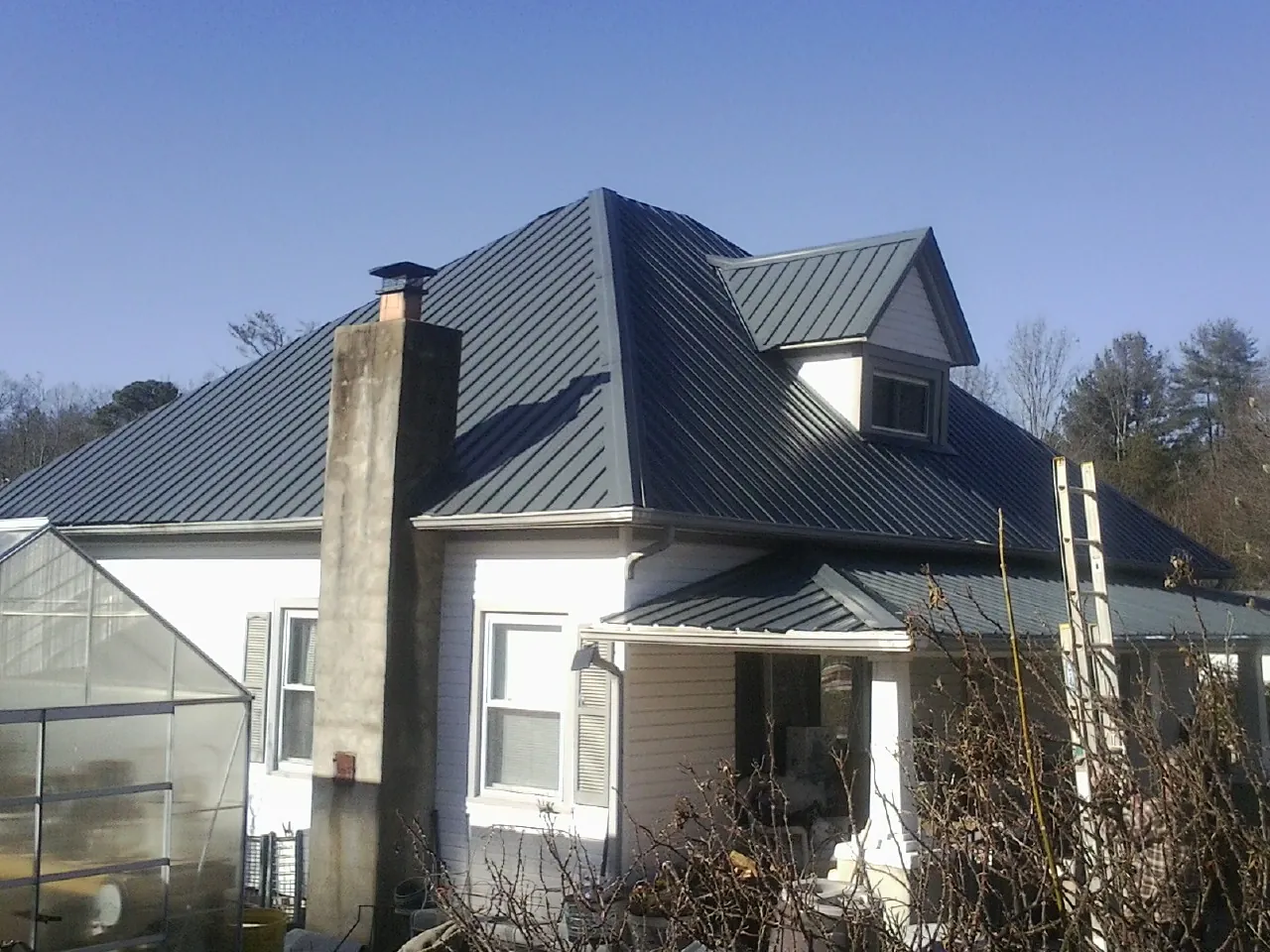 Dark blue standing seam metal roof on a white farmhouse with dormer in Guilford