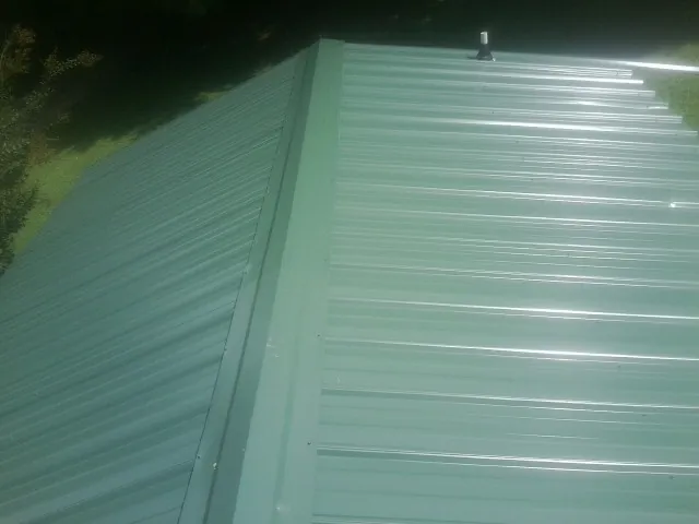 New green metal panels meeting at the ridge of a roof — Flat Roof Repair work by our crew in Guilford