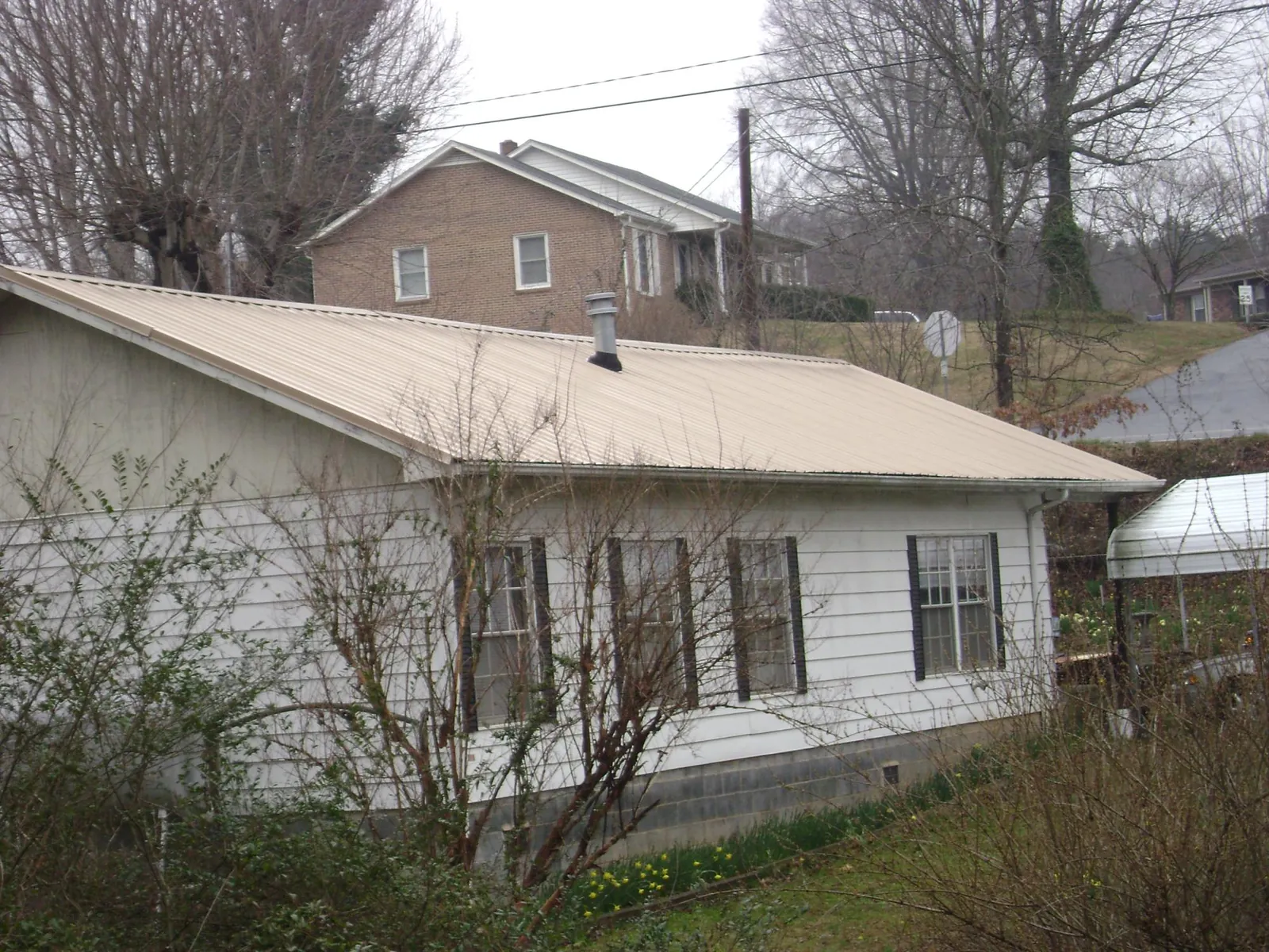 Tan metal roof on a white sided house set into a hillside — Commercial Roofing by Roofing Brothers in Guilford